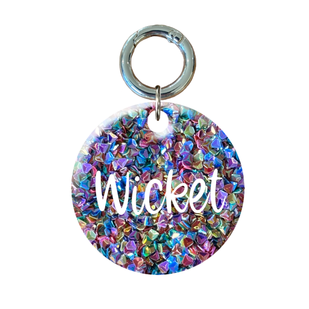 Round glitter dog tag with colorful crystal pattern and 'Wicket' engraved in white letters