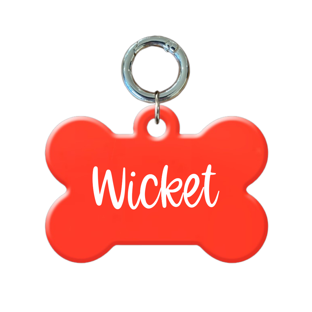 Red bone-shaped dog tag with metal ring, personalized with the name 'Wicket' in white text