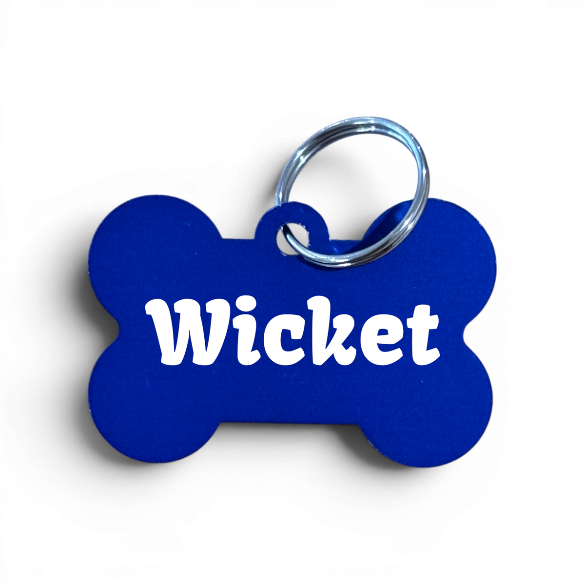A bone-shaped blue pet ID tag with the name 'Wicket' printed in white, attached to a silver metal key ring, shown on a white background.