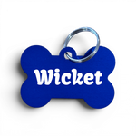 A bone-shaped blue pet ID tag with the name 'Wicket' printed in white, attached to a silver metal key ring, shown on a white background.