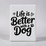 A white rectangular decorative magnet with rounded corners featuring the phrase 'Life is Better with a Dog' in black script and serif lettering, accented with small heart and paw print icons, shown against a neutral gray background.