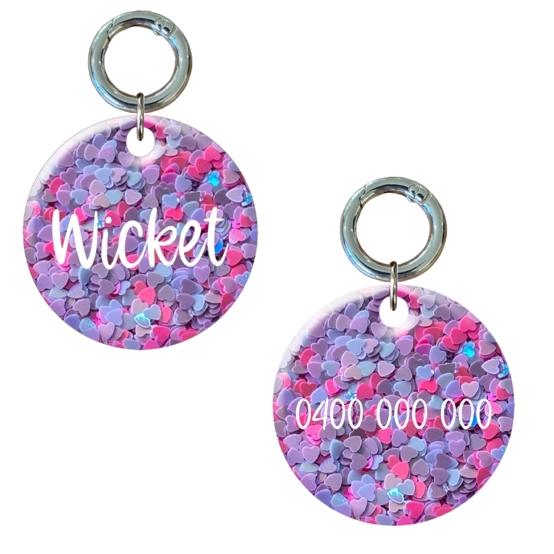 Round dog tag with pink and purple heart pattern, personalised with name and phone number.