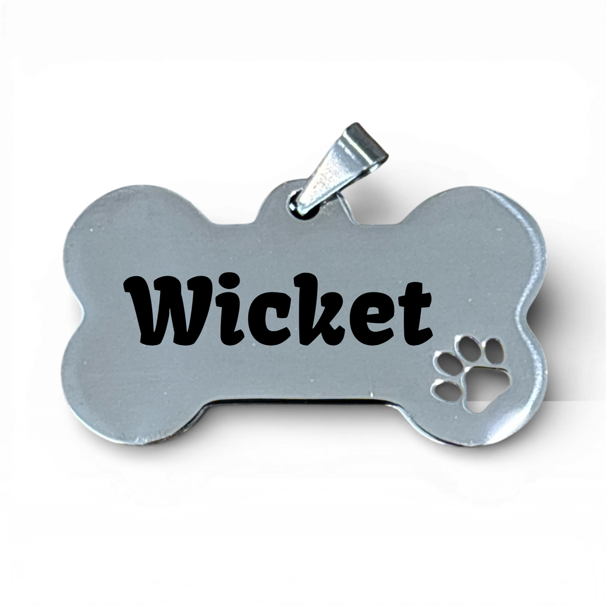 Stainless steel bone-shaped dog tag with 'Wicket' engraved and a paw print cutout.