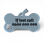Stainless steel bone-shaped dog tag with engraved text and paw cutout on white background.